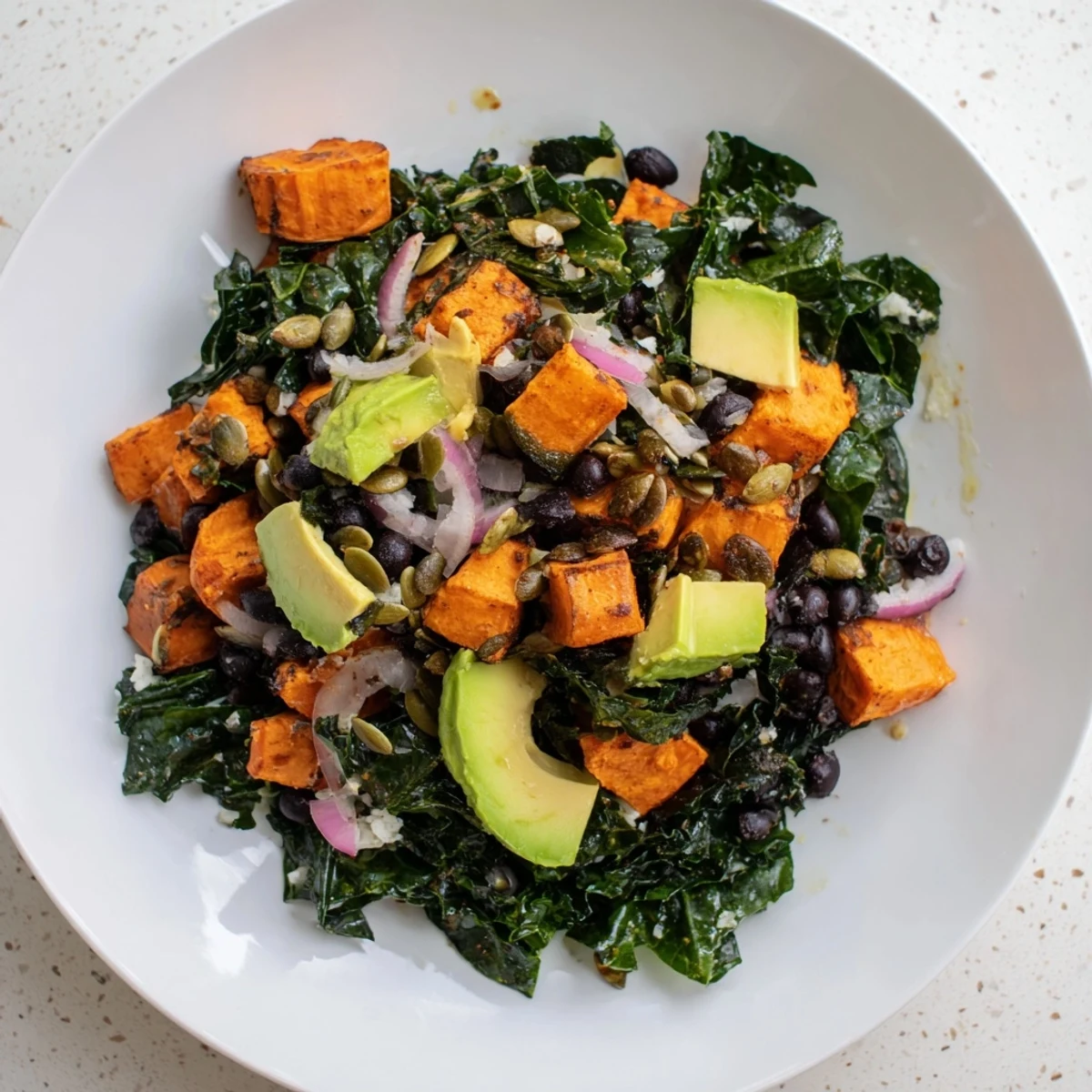 Close-up of a colorful massaged kale salad with roasted sweet potato and creamy avocado.