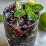 Close-up of a Black Currant Mojito showing muddled mint leaves and purple black currant jam swirled into the drink.