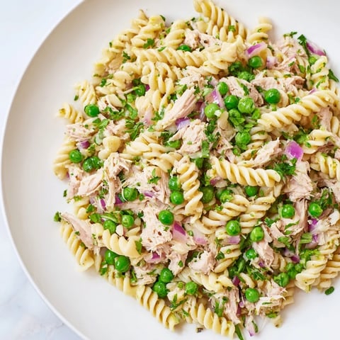 Freshly cooked fusilli pasta mixed with tender peas and flaked tuna, tossed in a bright lemon-herb dressing in a rustic white bowl.