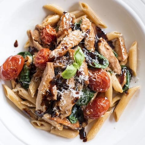 A vibrant plate of balsamic glazed chicken pasta features spinach leaves, melted Parmesan, and a glossy, herb-infused sauce ready to serve.  
