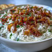 Creamy caramelized onion dip with Greek yogurt base served in a white bowl, garnished with fresh chives and paired with crispy potato chips.